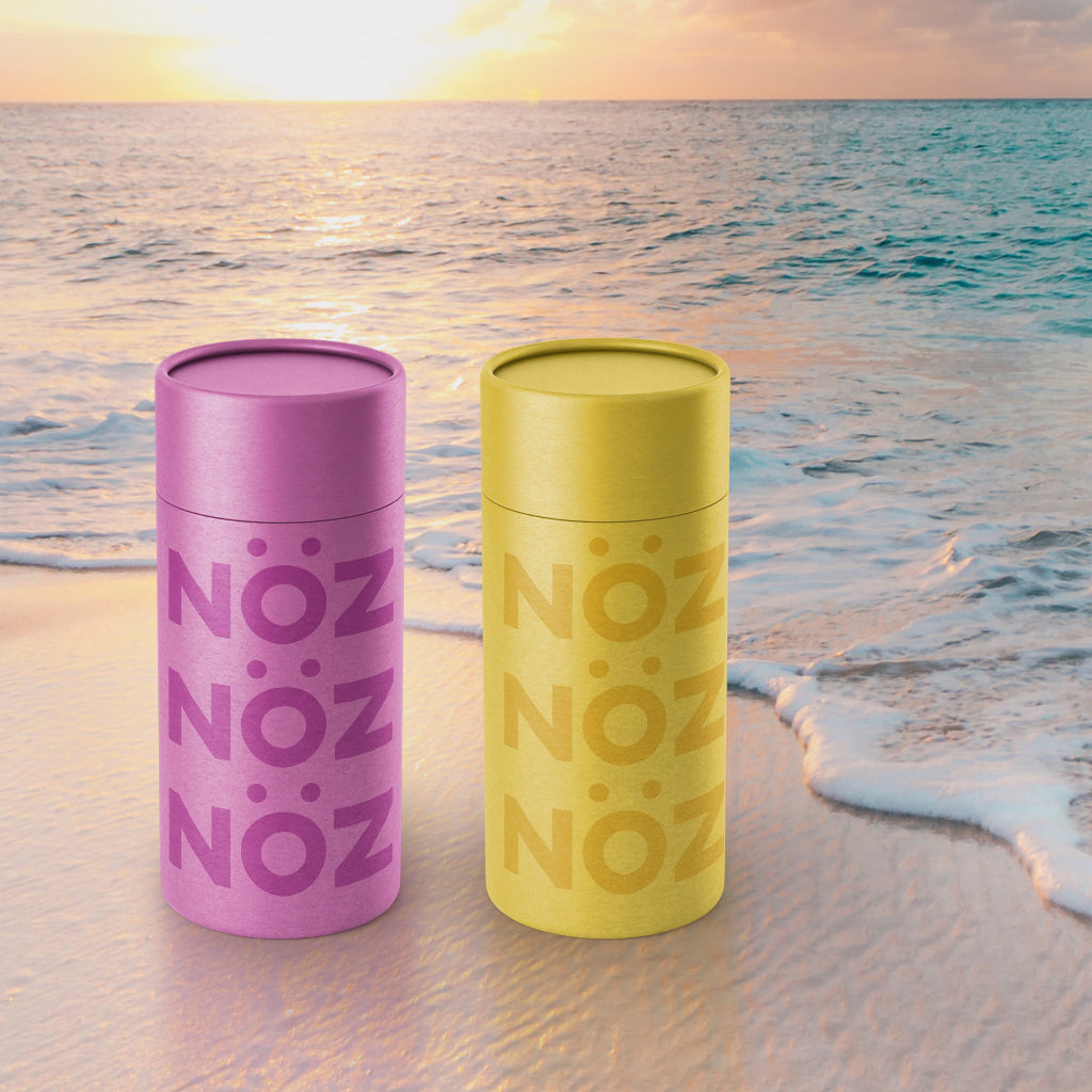 purple and yellow Noz sunscreen tubes sitting in front of a breaching wave